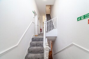 A staircase with a fire exit sign, white walls, and a carpeted floor. - Modern Studio Flat,Great Location Finsbury Park (Greater London)