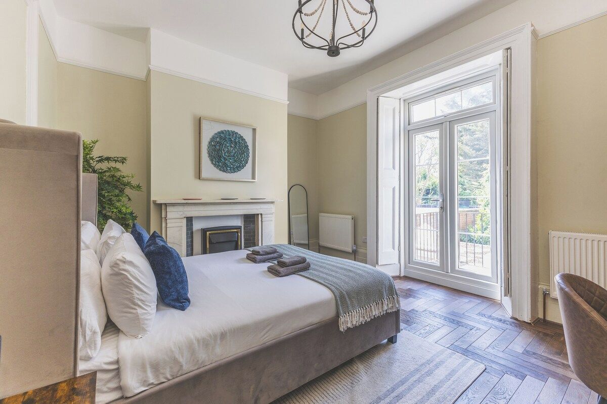 A bedroom with a bed, a fireplace, a large window, and a chair.