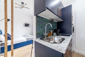 Ein kompaktes Zimmer mit einem Bett, einer kleinen Küchenzeile mit Spüle und einem Fernseher.