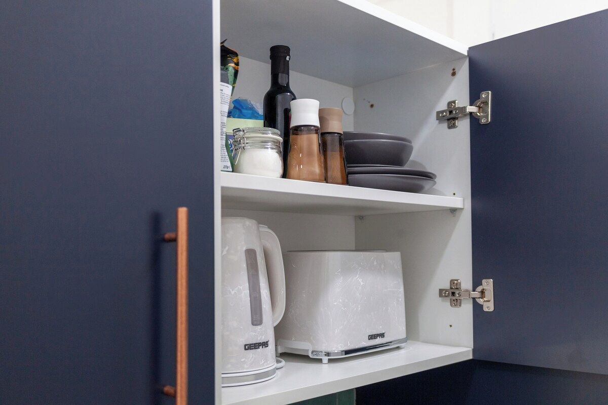 Et køkkenskab med en GEERPS-toaster, en GEERPS-kedel, en flaske og et glas.