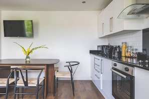 A modern kitchen with a dining area, a flat-screen TV mounted on the wall, and a vase with yellow flowers on the table. - Spacious 3Bed 3Bath Hackney Downs, 3min to Station (London)