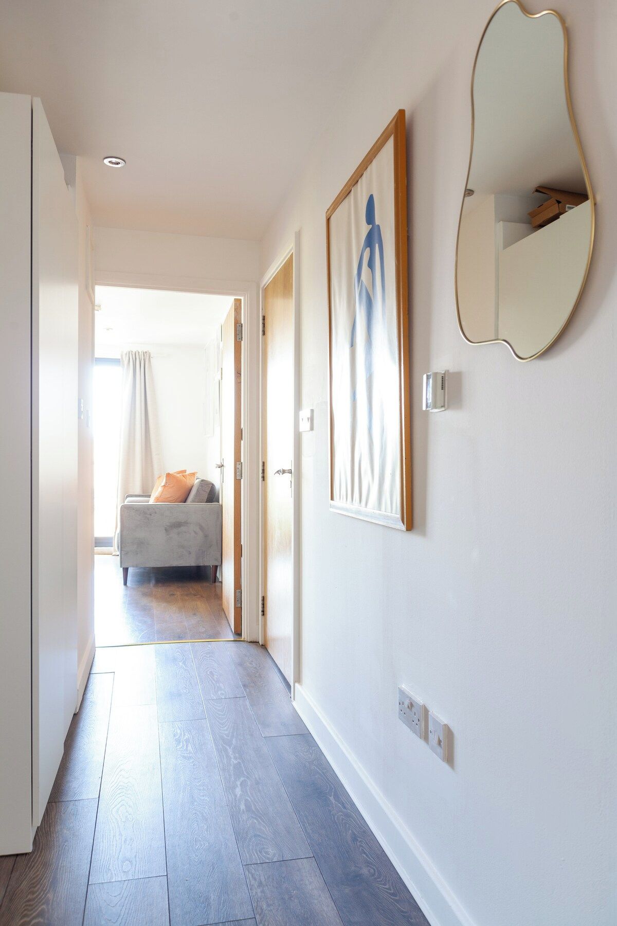 Un couloir avec un canapé, un tableau et un miroir au mur.