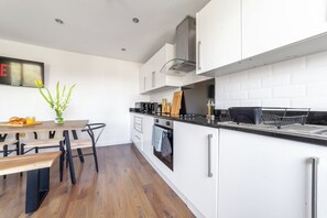 A modern kitchen with white cabinetry, a wooden countertop, and a dining area with a bench. - Spacious 3Bed 3Bath Hackney Downs, 3min to Station (London)