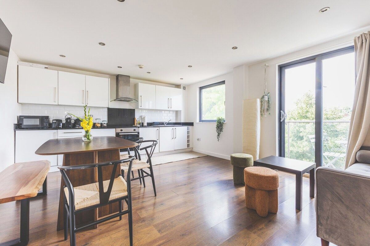 A modern kitchen with white cabinets, a dining table with chairs, and a large window providing a view of greenery.