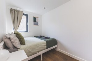 A single bed with a headboard, a bedside table, a window with curtains, and a wall-mounted artwork. - Spacious 3Bed 3Bath Hackney Downs, 3min to Station (London)