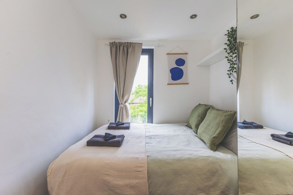 Un dormitorio con cama, cortinas, una planta colgante y una obra de arte en la pared.