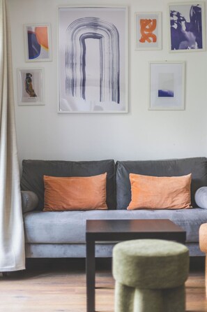 Una sala de estar con un sofá gris, cojines naranjas y un otoman verde.