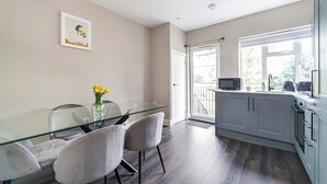 A modern kitchen with a glass dining table, grey cabinets, and a view to the outside. - Lovely 2BR Flat, 15Minutes to Wembley, Sleeps 5ppl (Greater London)
