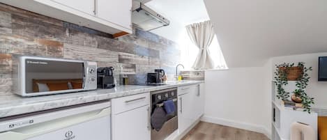 A modern kitchen with white cabinetry, a built-in microwave, a dishwasher, and a window with curtains.