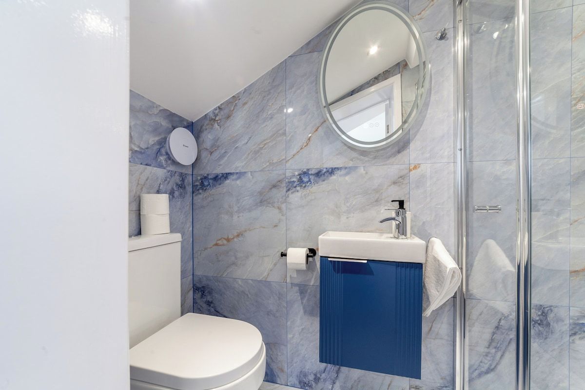 Un bagno con il water, un lavabo con mobiletto blu, box doccia in vetro e parete in marmo.