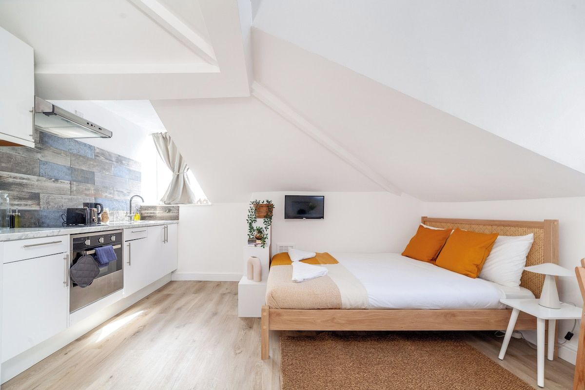 A modern, compact bedroom with a wooden bed, a bedside table, and a TV mounted on the wall.