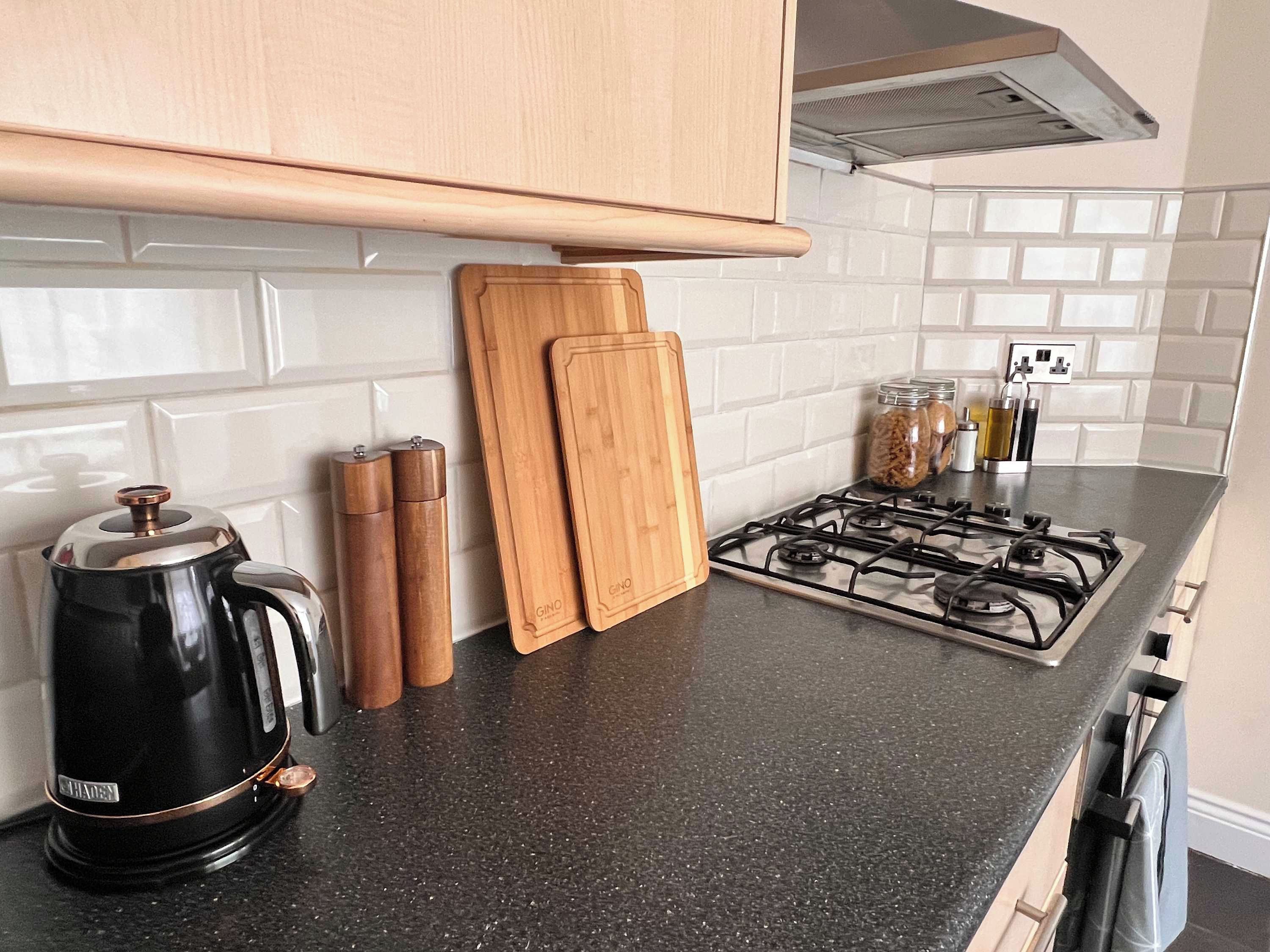 Una cocina con estufa a gas, cafetera, tablas de cortar de madera y un estante para especias.