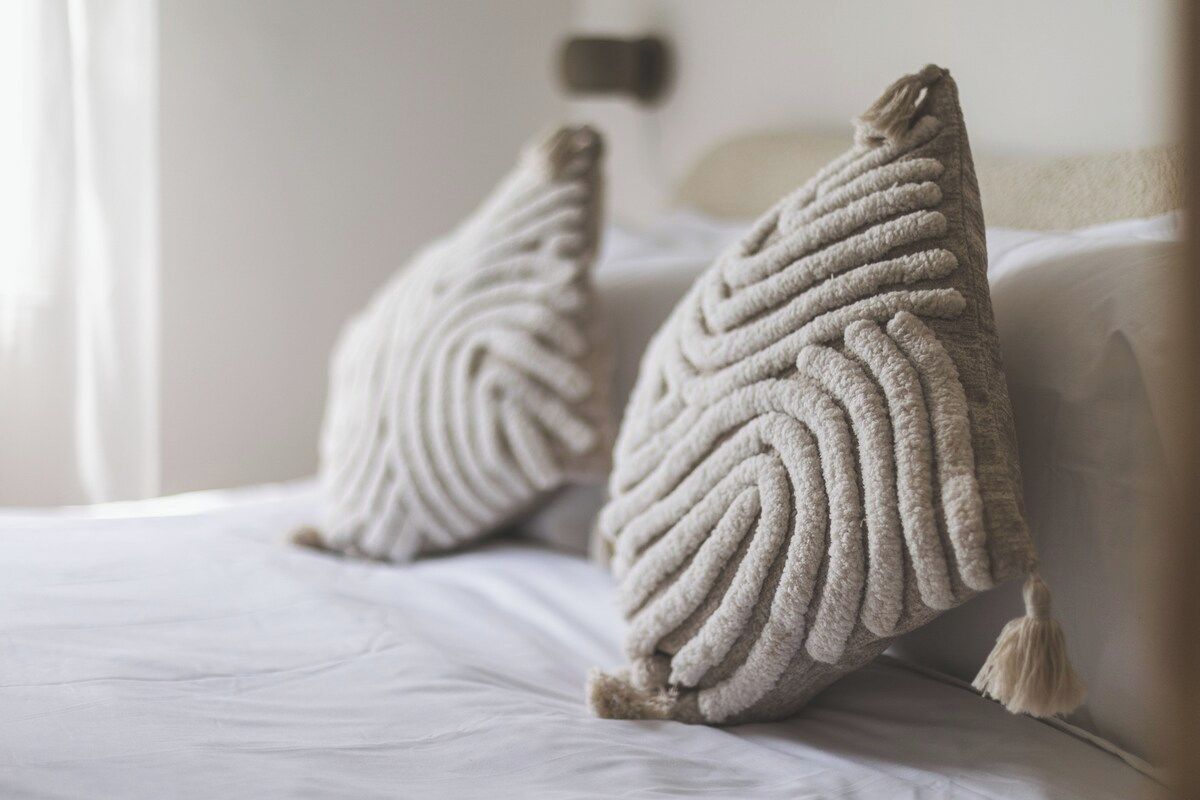 Un lit avec deux oreillers à texture et une tête de lit blanche.