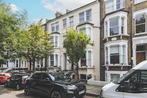 A row of terraced houses with parked cars and a white van on the street. - Stunning Studio Flat Highbury - GREAT Location (Greater London)