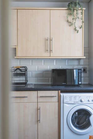 A kitchen with wooden cabinets, a microwave, a toaster, and a washing machine. - Modern Garden House Stratford FREE Street Parking (Greater London)