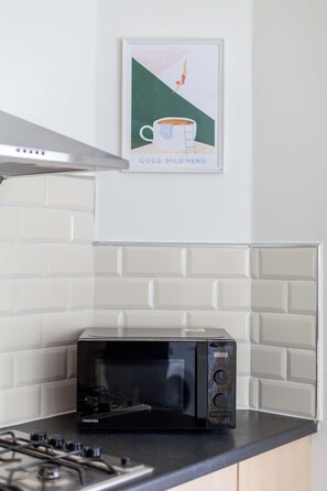 A kitchen with a microwave on the counter, a stove, and a wall-mounted picture. - Modern Garden House Stratford FREE Street Parking (Greater London)
