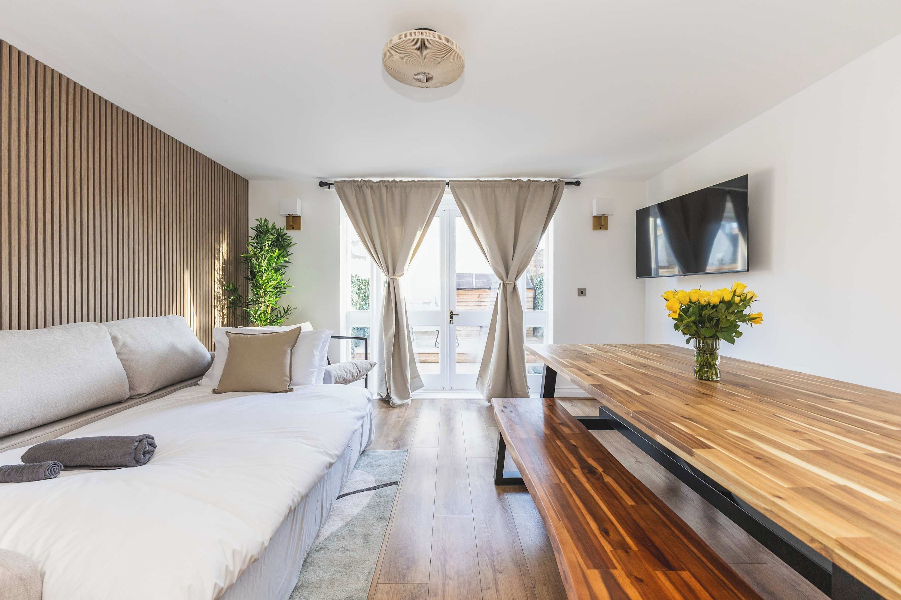 Une chambre moderne avec un lit, un banc en bois, une télévision et une fenêtre avec des rideaux.