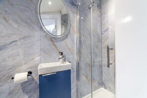 A bathroom with a marble wall, a glass shower enclosure, and a sink with a mirror above it. - Cozy Studio, Close to Arsenal Finsbury Park (Greater London)