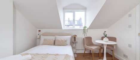 A bedroom with a bed, bedside table, chair, and a small table with a plant.