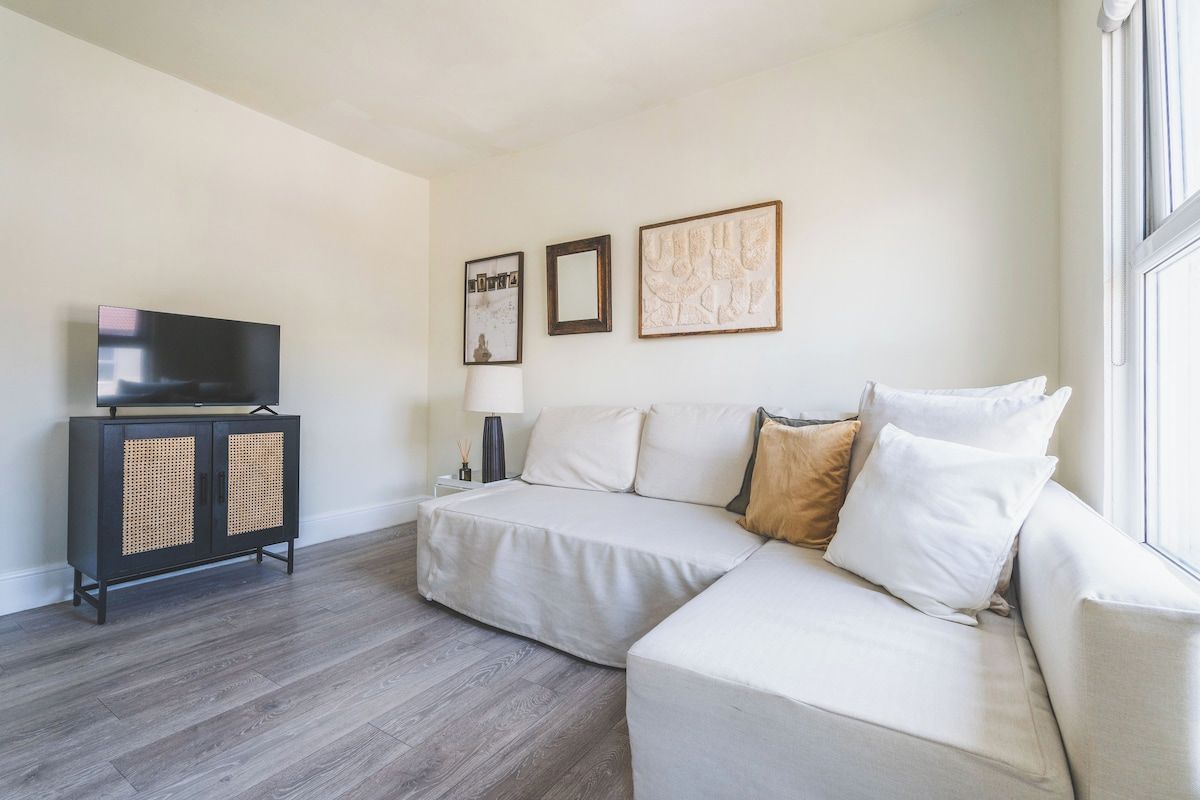 Una sala de estar con un sofá modular, un televisor sobre un mueble bajo y cuadros en la pared.