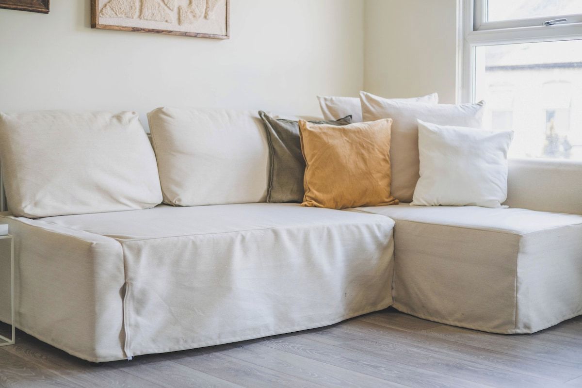 A sectional sofa with multiple cushions in a room with wooden flooring and a window.