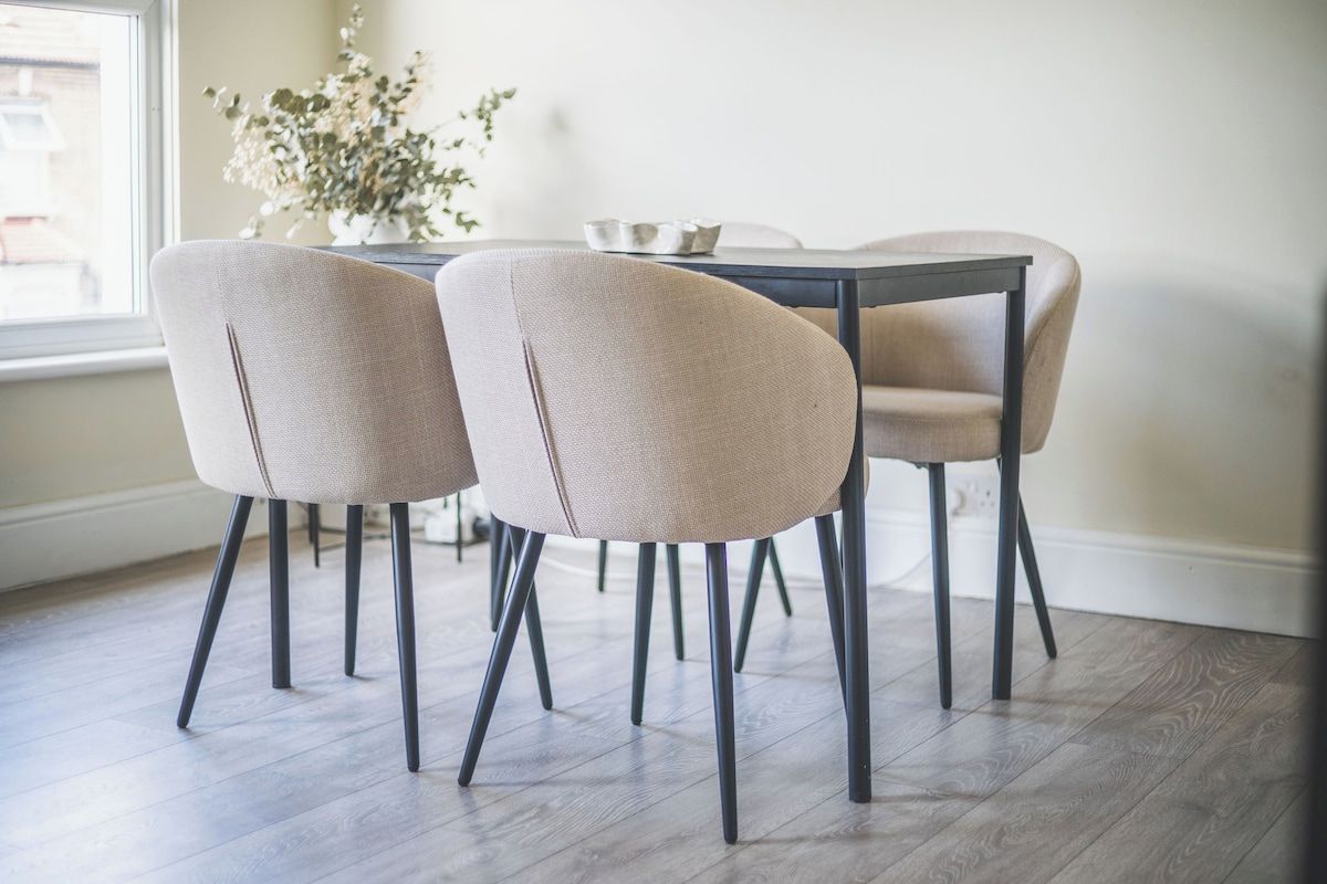 Uma sala de jantar com uma mesa redonda e quatro cadeiras de pernas escuras.