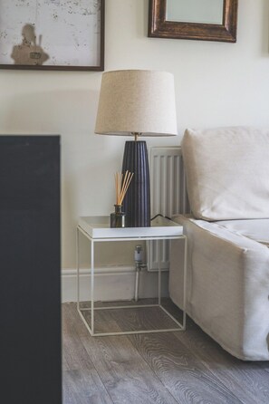 A modern living room with a white sofa, a side table with a lamp, and a radiator. - 2 Bed| Sleeps 6|2 min Central line tube|Abba Arena (Greater London)