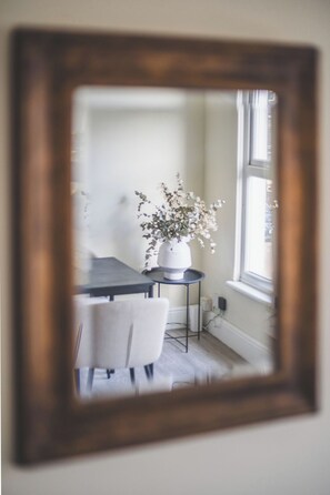 Ein Zimmer mit Esstisch, einem Sessel, einem kleinen runden Tisch mit Topfpflanze und einem Fenster.