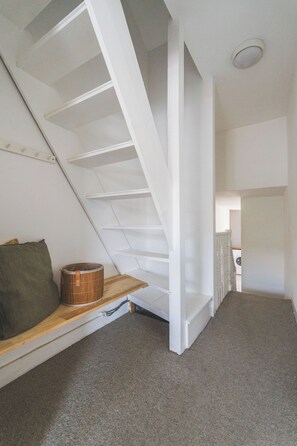 A room with a sloped ceiling, a wooden bench, a green pillow, and a white staircase. - 2 Bed| Sleeps 6|2 min Central line tube|Abba Arena (Greater London)