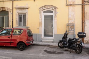 Ein rotes Auto parkt auf einer Straße vor einem gelben Gebäude mit einer weißen Tür und Rundbogenfenstern.