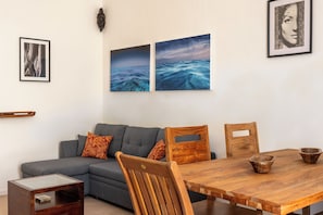 Ein modernes Wohnzimmer mit grauem Sofa, Holzstühlen, einem Holzessttisch und Kunstwerken an den Wänden.