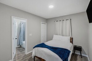 Ein Schlafzimmer mit Bett, Nachttisch, einer Tür und einer Dusche.