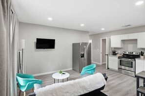 A modern kitchen with stainless steel appliances, a dining area with two chairs, and a flat-screen TV mounted on the wall. - Cozy 3BR Duplex Laundry Min to Downtown (San Antonio)