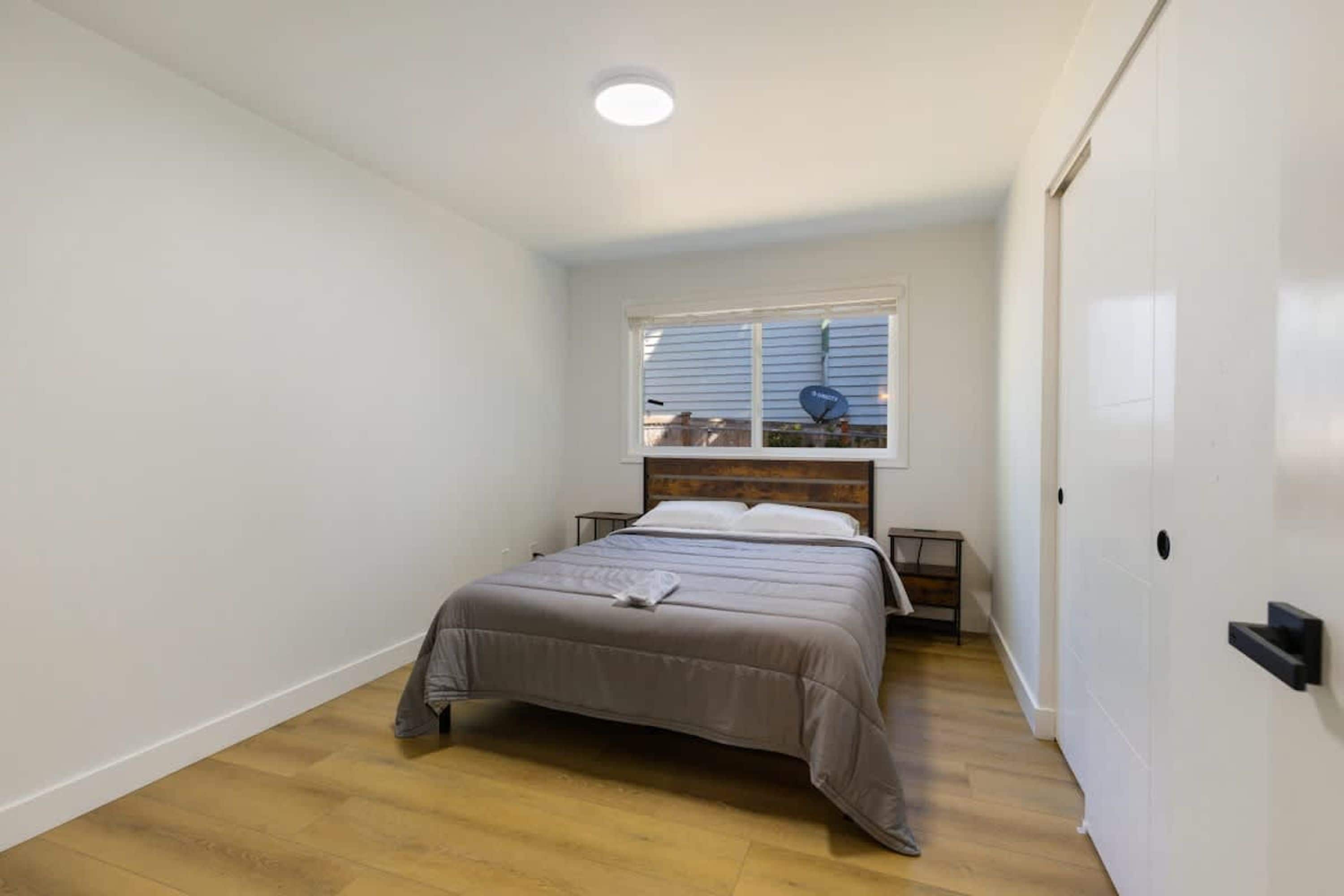 A bedroom with a bed, a window, a bedside table, and a wardrobe.