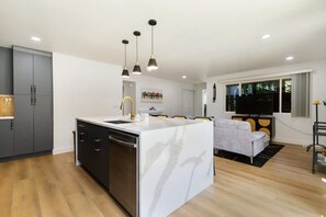 Una cocina moderna con una isla central, un área de comedor con sofá y un televisor en la sala de estar.