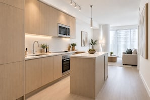 Una cocina moderna con armarios de madera, microondas integrado y una isla central con un bol de fruta.