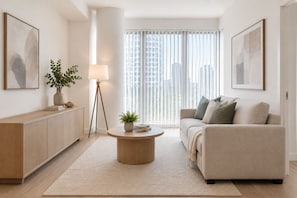 Una sala de estar moderna con un sofá, una mesa de centro, una lámpara y vistas de la ciudad a través de amplios ventanales.