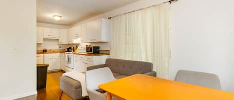 Un espacio habitable compacto con kitchenette, un comedor con mesa y sillas, y un sofá.