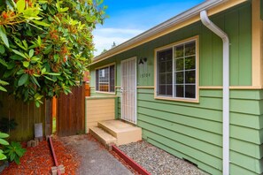 A green house with a door labeled '15104,' a small porch, and a wooden fence. - Cozy 2BR Home in Lynnwood w Backyard (Lynnwood)
