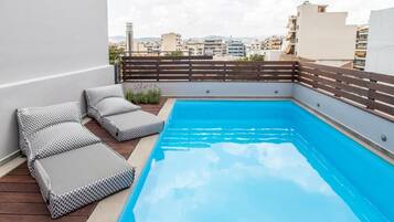 A rooftop pool with a wooden deck, lounge chairs, and a view of the cityscape.