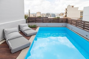 A rooftop pool with a wooden deck, lounge chairs, and a view of the cityscape. - Citylinkers Suites (Athina)