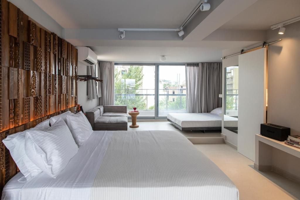A hotel room with a large bed, a sofa, a small table, and a balcony with a view.