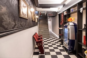 A hallway with a checkered floor, a red chair with 'ZA' on it, a vending machine, and a staircase in the background. - Citylinkers Suites (Athina)