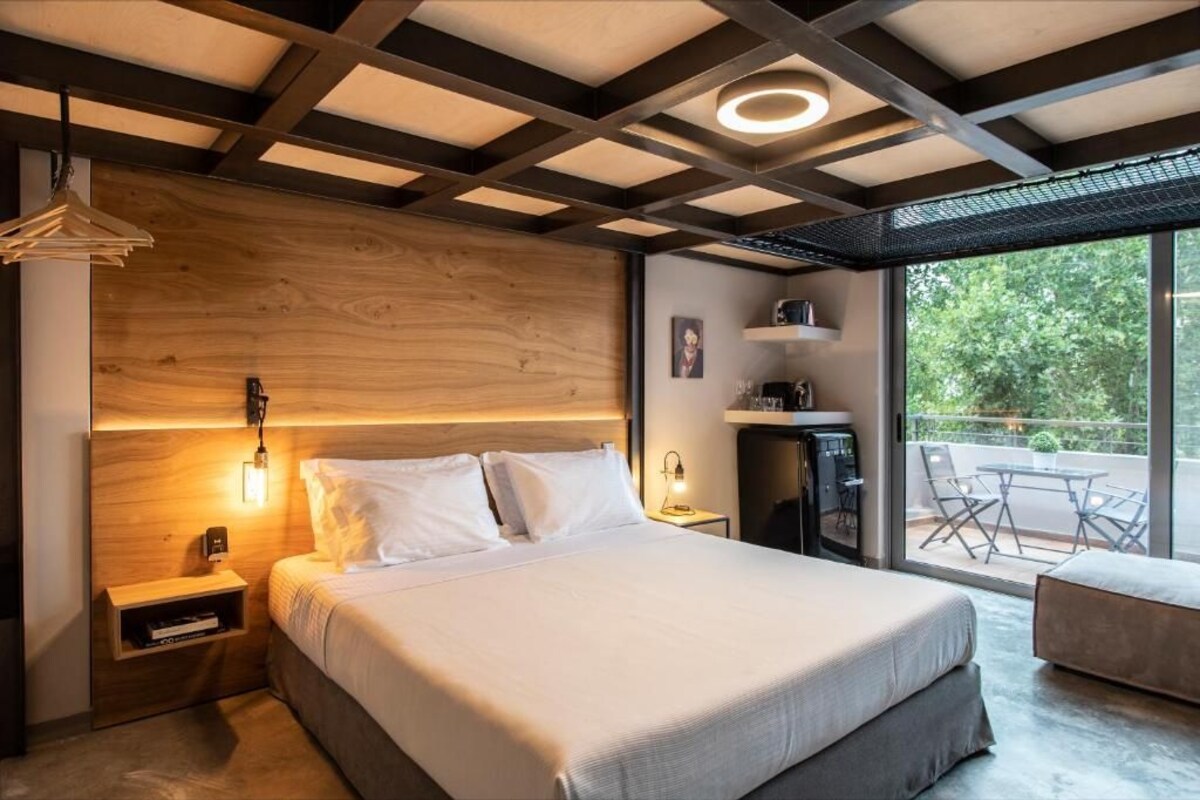 A modern bedroom with a large bed, bedside tables, a nightstand, a desk, and a balcony with outdoor seating.