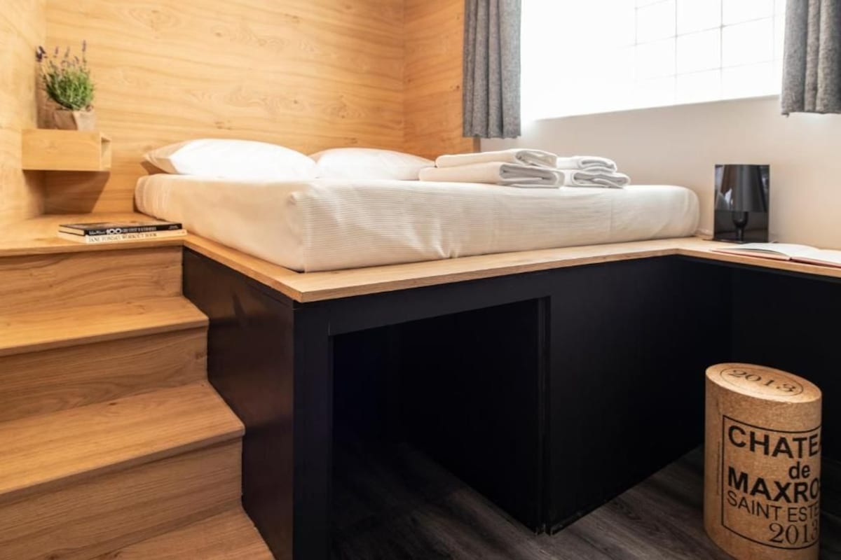 A modern room with a bed, a small desk, a lamp, and a bottle of wine.