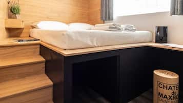 A modern room with a bed, a small desk, a lamp, and a bottle of wine.