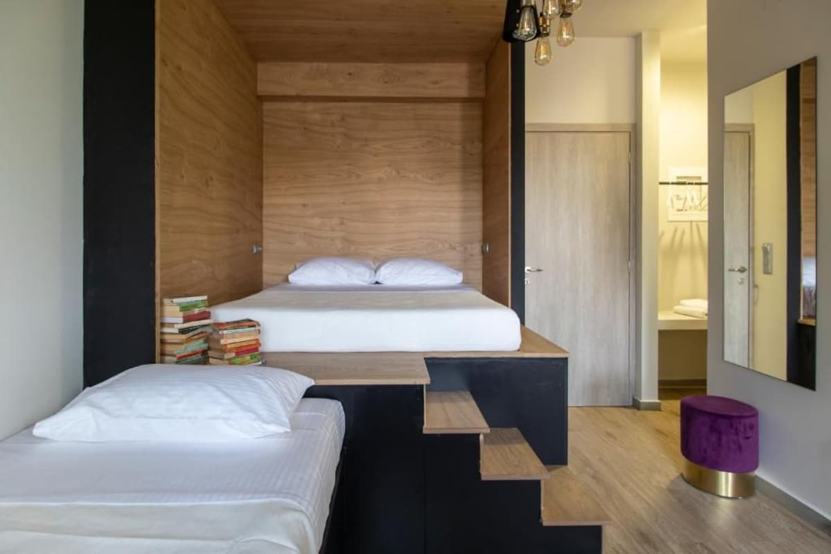 A bedroom with a bed, a bedside table, a stack of books, and a small stool.