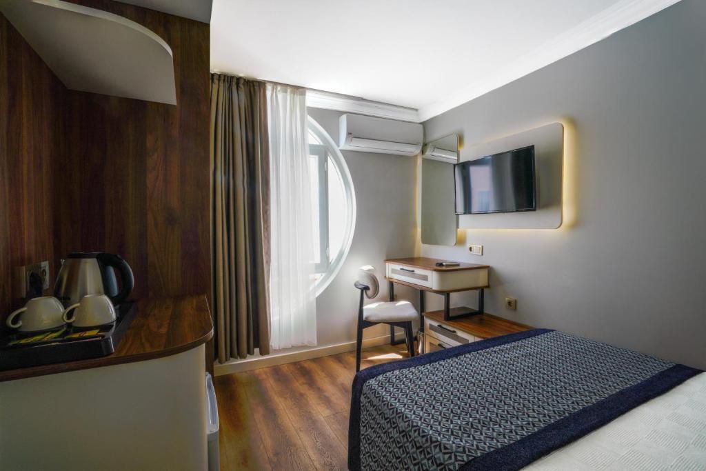 Habitación de hotel con cama, escritorio, silla, televisor montado en la pared y ventana con cortinas.