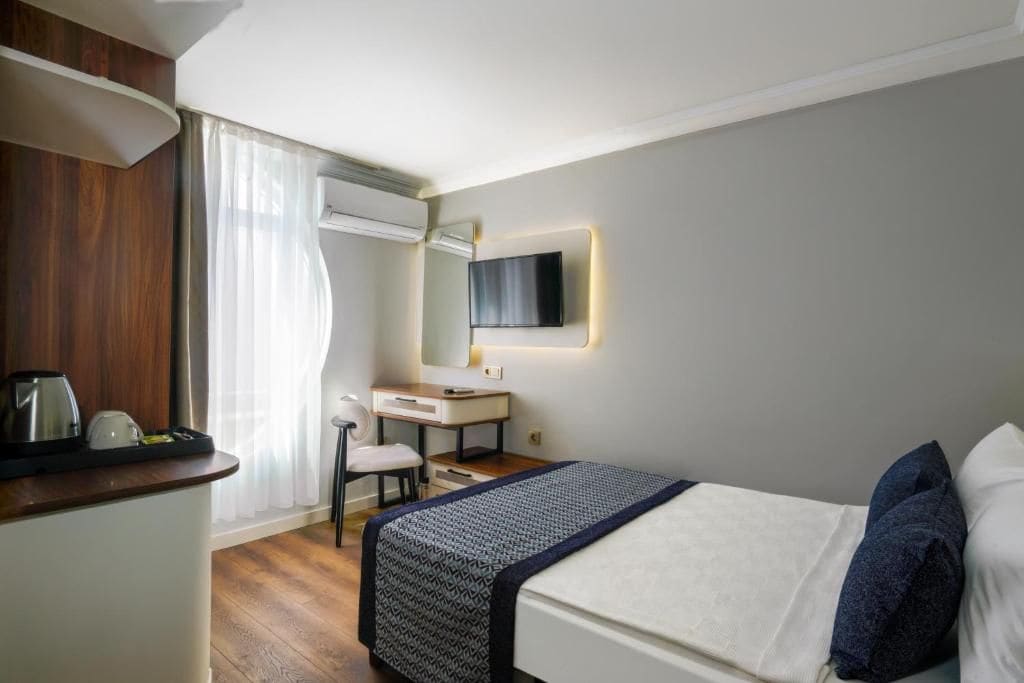 A hotel room with a bed, a desk, a chair, a television, and a window with curtains.