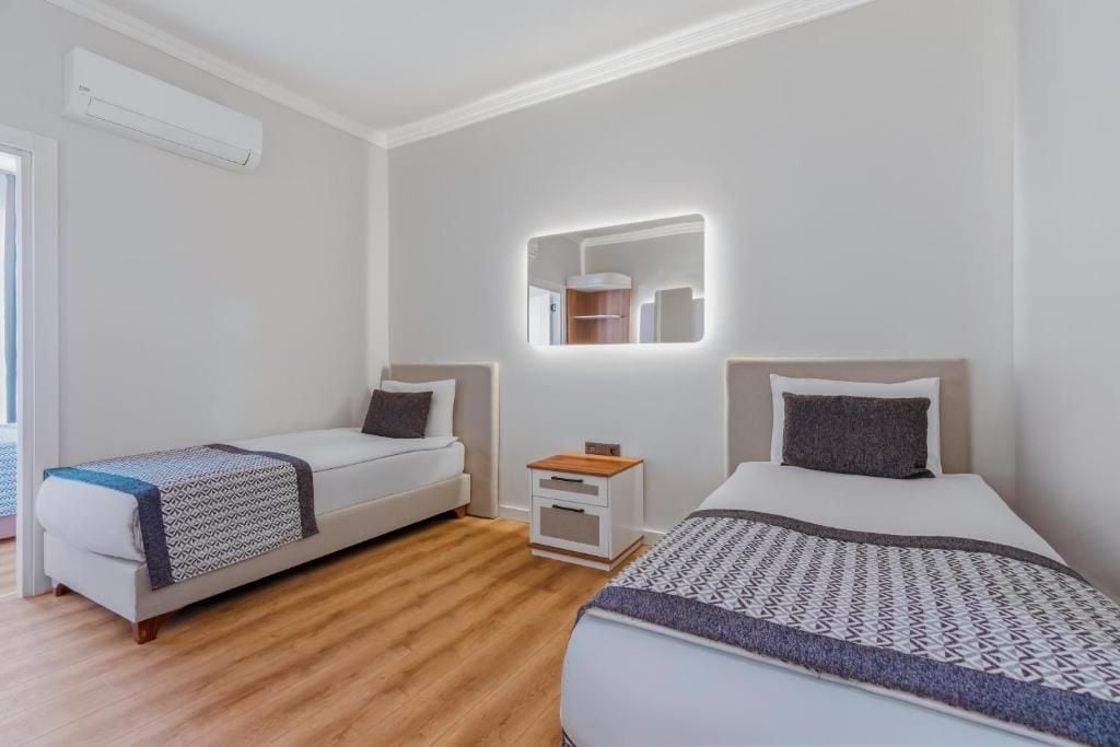 Een moderne hotelkamer met twee enkele bedden, een klein nachtkastje en een spiegel erboven.